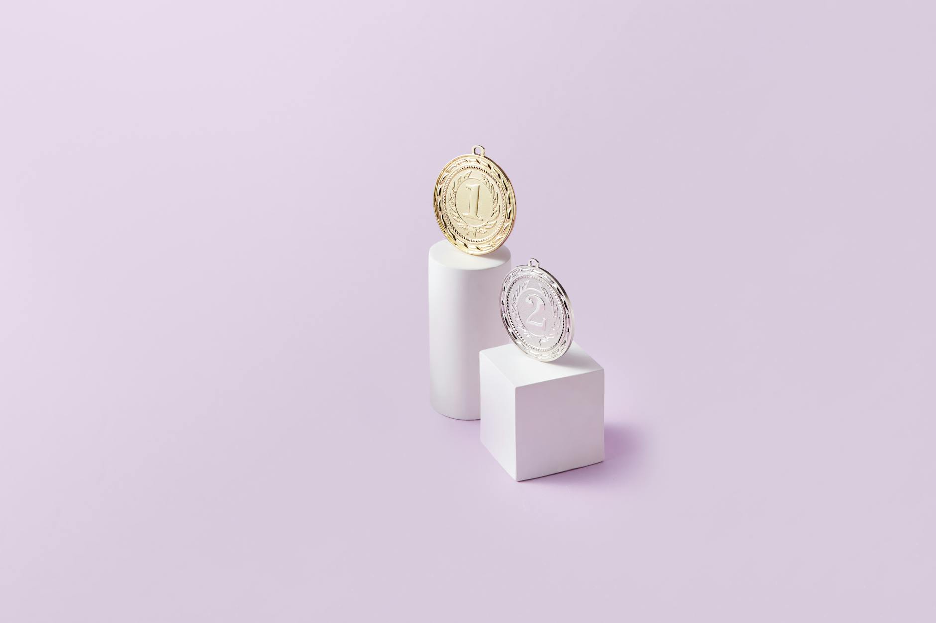 Złoty i srebrny medal na białych podium na różowym tle