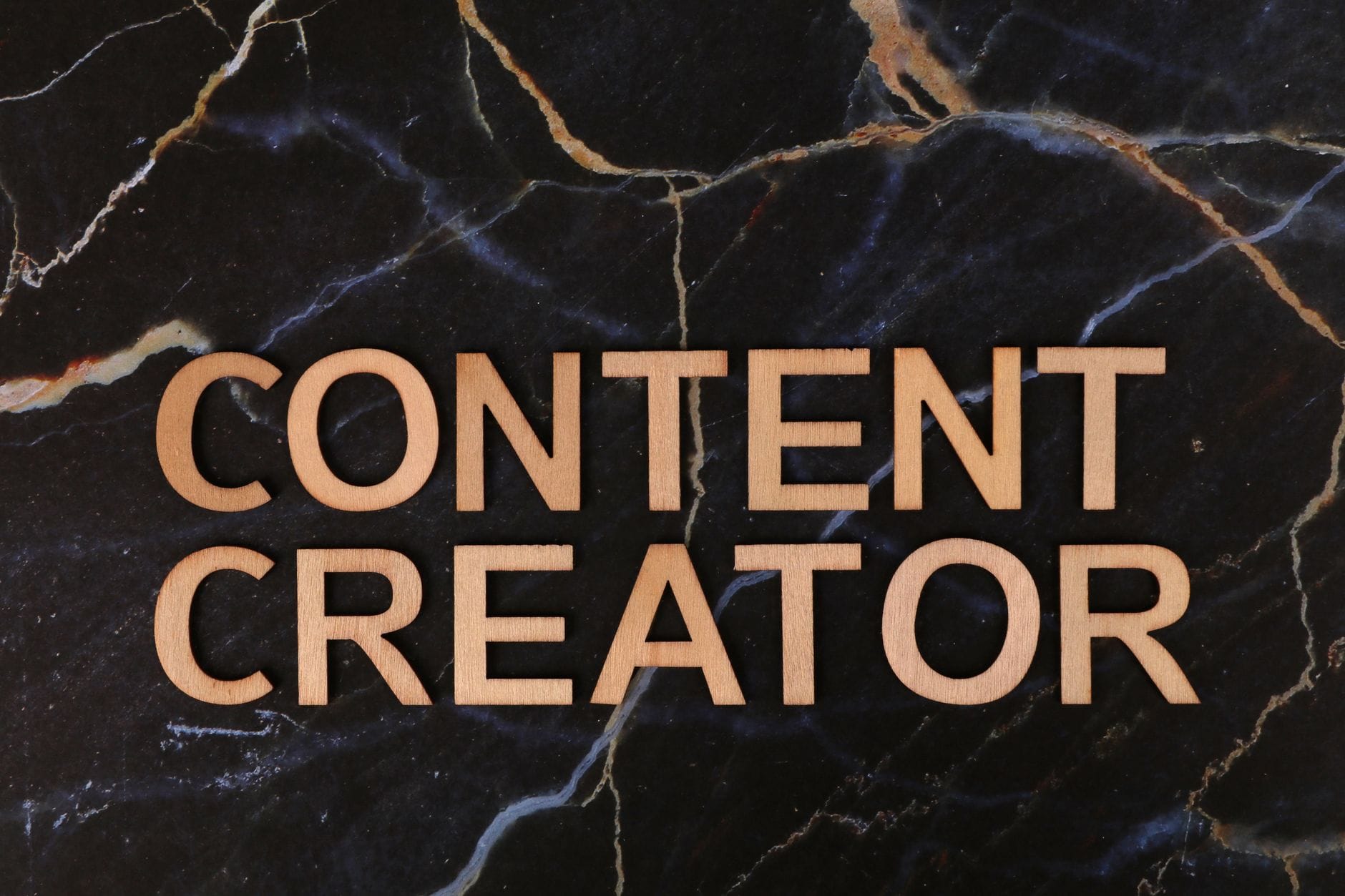 Drewniane litery układające się w napis CONTENT CREATOR na marmurze